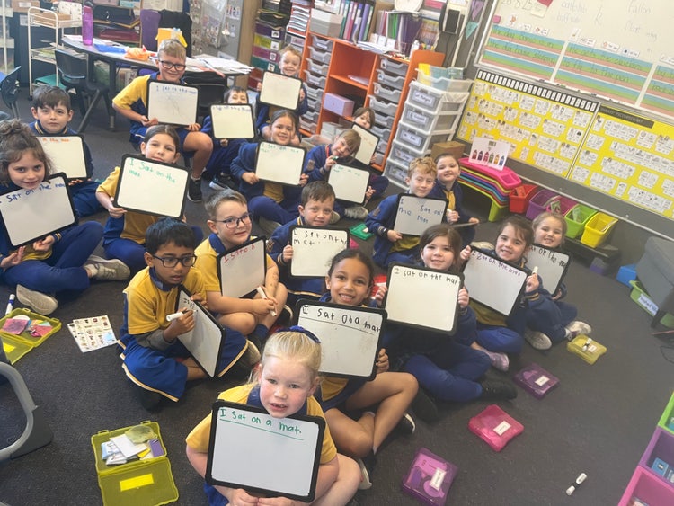 Students engaging in whole-class literacy activities, using individual whiteboards for writing.